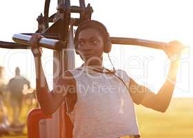 Staying fit and strong. A young woman using outdoor exercise equipment at the park.