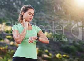 Getting more fit by the day. Shot of a young woman checking her heart rate while exercising outdoors.