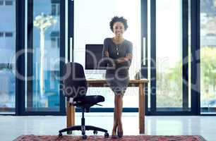 Allow me to share my success story with you. Portrait of a confident young businesswoman leaning against a desk at work.