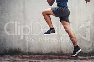 Set off to the finishing line. Closeup shot of an unrecognizable man running against a grey wall outdoors.