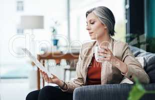 To get through paperwork, one must have coffee. Cropped shot of an attractive mature businesswoman sitting alone and enjoying a cup of coffee while reading paperwork.