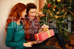 Sharing Christmas with someone special. Shot of a young man opening his christmas present while sitting with his girlfriend.