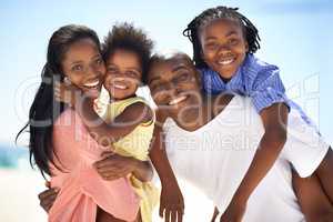 Carrying their happy kids at the beach. Two parents giving their children a piggyback while on the beach.