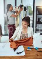 Doing their jobs perfectly. Shot of a young fashion designer sewing garments while a colleague works on a mannequin in the background.