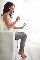 What to browse today. Shot of a young woman using her tablet while relaxing on the sofa at home.