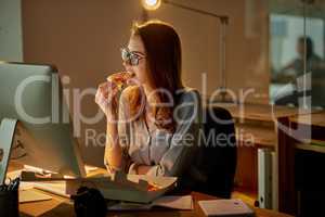 Late night meals in the office. Shot of an attractive young businesswoman eating pizza while working late in the office.