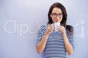 Now thats a fine brew. Portrait of a an attractive woman holding a coffee cup against a gray background.