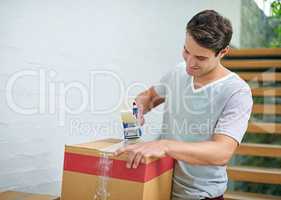 Sealing up the last few boxes. Shot of a young man packing up his belongings into boxes before moving out.