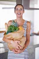 A healthy life is a happy life. An attractive woman holding a bag of groceries in the kitchen.