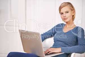 Browsing the news feed. Portrait of a beautiful woman sitting on a chair using a laptop.