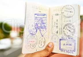 Every stamp tells a story. Shot of an unidentifiable young man holding open a passport full of visa stamps.