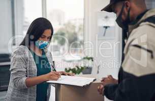 Everything is perfectly in order. Shot of a masked young woman signing for a delivery received at home.