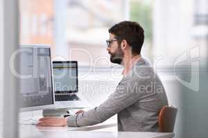 Focusing on the finer details. Shot of a handsome young man working on a computer in a casual working environment.