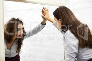 Low self esteem. Attractive young woman looking in a mirror and seeing a hideous reflection.