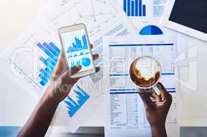 Coffee makes the business world go round. High angle shot of an unidentifiable businesswoman drinking coffee while analyzing graphs on her smartphone.