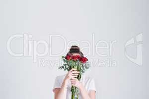 Love passionately like a red rose. Studio shot of an unrecognizable woman covering her face with flowers against a grey background.