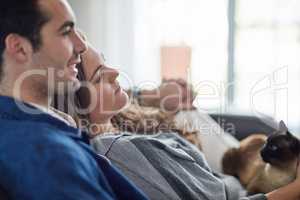 Homely bliss at its best. Shot of a happy young couple relaxing on the sofa at home with their cat.