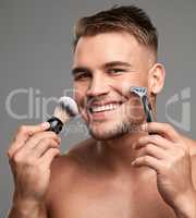 Guess whos getting rid of the beard. Studio shot of a handsome young man holding a razor and brush against a grey background.