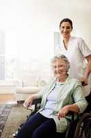 Youre in good hands with her. Portrait of a smiling caregiver and a senior woman in a wheelchair at home.