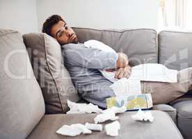 Anyone want to trade places. Portrait of a sickly young man holding a pillow while sitting on a couch with tissues laying all around at home.