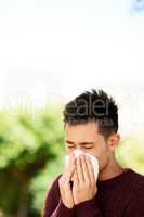 Its allergy season. Cropped shot of a young man blowing his nose outside.