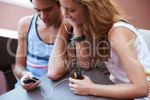 Get closer to your crush through the wonders of technology. Happy teen couple sharing an MP3 player and listening to music while enjoying their beverages.