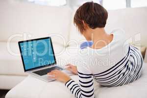 Rear view of a young woman working on her laptop while relaxing at home- ALL screen content on this image is created from scratch by Yuri Arcurs team of professionals for this particular photo shoot