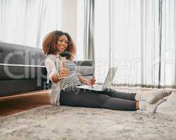 Ive bought all the things I need. Portrait of a cheerful young woman doing online shopping on her laptop while being seated on the floor at home.
