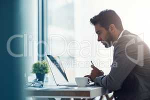 Focus and intention will get you far. Shot of a handsome young businessman using a laptop and cellphone at his desk in a modern office.