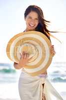 Sun-kissed beauty. A beautiful young woman wearing a sarong and holding a woven sunhat at the beach.