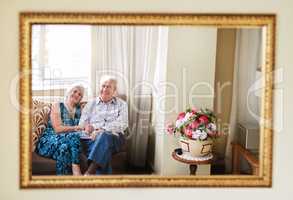 Their love is a reflection of their life. Portrait of a happy senior couple relaxing on the sofa together at home reflected in a mirror.