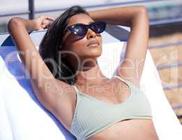 Poolside is where I belong. Shot of a young woman relaxing on a lounger by the poolside on a sunny day.