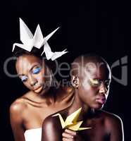 African fire and ice. Cropped shot of two beautiful ethnic women posing with origami against a black background.