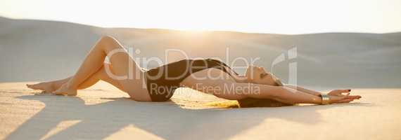 Freedom and isolation on the beach. Shot of a beautiful young woman in swimwear lying on the sand at sunset.