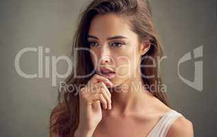 Thoughts of a beauty. Studio shot of an attractive young woman standing against a brown background.