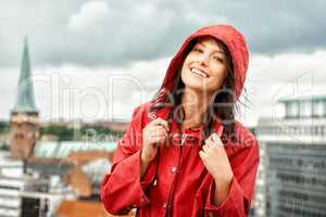 A rainy day cant get her down. Pretty young woman smiling while wearing a red raincoat - portrait.