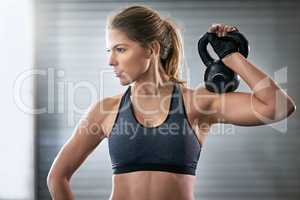 Building her upper body strength. Shot of a young woman working out with a kettle bell at the gym.