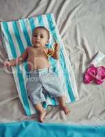 Excuse me while I get my beach on. Concept shot of an adorable baby boy lying on a towel at a make believe beach.