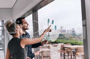 Envisioning the success they hope to achieve. Shot of two businesspeople brainstorming on a glass wall in an office.