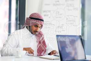 Staying on task with smart technology. Shot of a young muslim businessman using a digital tablet at his work desk.