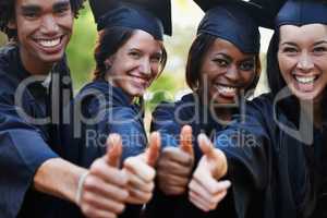 Get educated. A group of smiling college graduates giving the thumbs up at graduation.