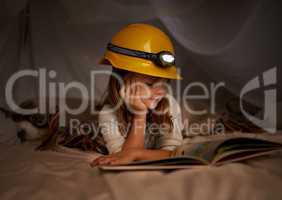 Books are the stepping stones of imagination. Shot of an adorable little girl using a headlight to read her book in a fort.