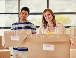 Heres to new beginnings.... Portrait of a smiling young couple carrying boxes on moving day.