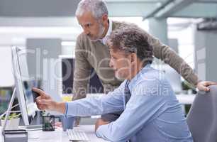 Theyre the senior partners on the project. A mature businessman sitting at his workstation explaining something to his colleague.
