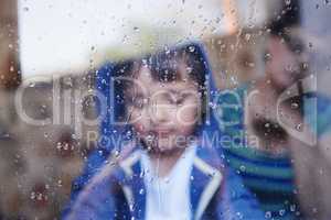 Rainy days with nothing to do.... A little boy looking downwards behind a rain-streaked window while his mother sits in the background.