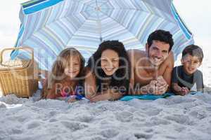 Enjoying a relaxing family vacation. A happy family smiling at the camera while lying under an umbrella at the beach.