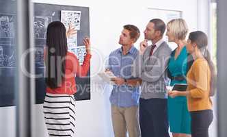 Inspiring her team. A businesswoman standing and presenting a storyboard to his team in an office.