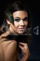 Feminine beauty. A gorgeous young woman with dramatic eye makeup holding a peacock feather.