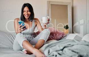 Mornings are for coffee and social media. Shot of a young woman using a smartphone and enjoying a cup of coffee in bed at home.