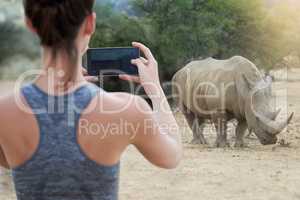 Immortalizing an unforgettable experience. Rearview shot of an unidentifiable young woman taking a picture of a rhinoceros in the wild.
